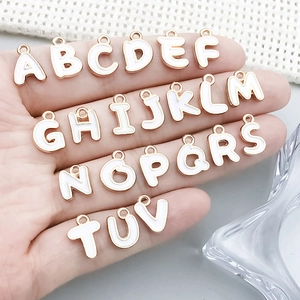 Hand hält weiße Emaille Buchstabenanhänger mit Roségoldlegierung für DIY-Schmuckherstellung