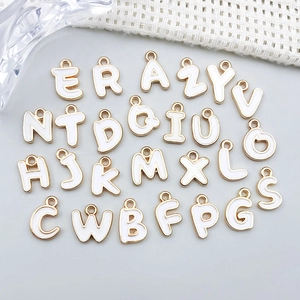 Nahaufnahme von 26 weißen Emaille-Buchstabenanhängern mit Goldrand für DIY-Schmuck