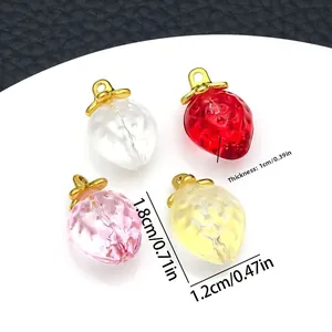Détail de breloques fraises en verre coloré avec boucles dorées sur socle blanc