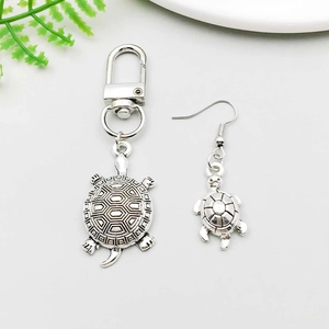 Detail of antique silver turtle keychain and matching earrings set on white background