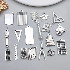 Détail macro de breloques scolaires en argent antique incluant règle et chapeau