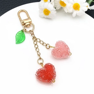 Detail of red and pink matte heart cherry pendants with golden keychain on white tray