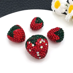 Macro detail of red and green rhinestone strawberry charms in various sizes for DIY jewelry