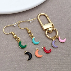 Detail of colorful enamel moon pendants on earrings and keychain against gray fabric