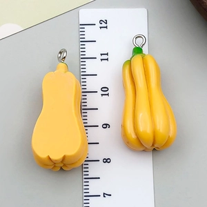 Vue détaillée des pendentifs citrouille en résine jaune avec anneaux et règle de mesure