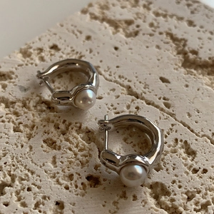 Irregular silver textured hoop earrings with white pearls on a neutral stone background