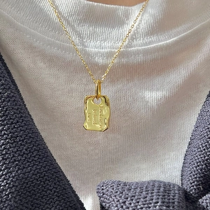 Goldene Halskette mit rechteckigem Anhänger und Gravur getragen von einem weiblichen Model