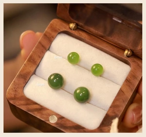 Primer plano de pendientes de jade Hetian verde de 6mm y 8mm sobre un joyero de madera