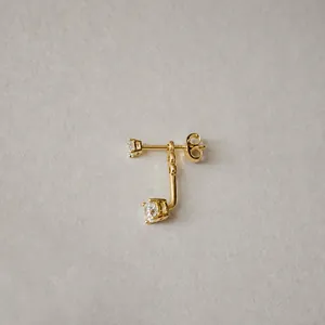 Detalle de pendientes de circonita bañados en oro de 18 quilates sobre fondo de papel texturizado