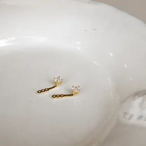 Vista de pendientes de botón dorados con circón y colgante curvo sobre cerámica blanca