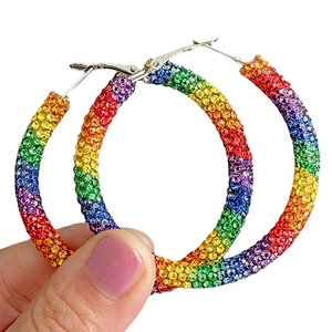 Détail de grandes créoles serties de strass arc-en-ciel colorés tenues à la main