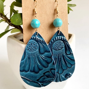 Détail de boucles d'oreilles en cuir bleu gaufré avec perles turquoise et crochets dorés