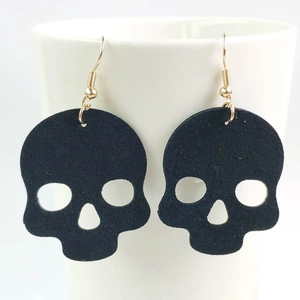 Detalle de pendientes de calavera negra en fieltro colgados de una taza blanca de cerámica