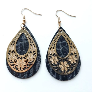 Detailed view of teardrop earrings with gold hollow floral metal and black textured leather