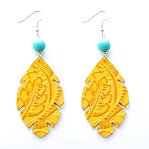 Détail de boucles d'oreilles bohèmes en cuir jaune gaufré avec une perle de turquoise