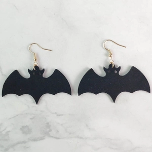 Pendientes de murciélago negro para Halloween con ganchos dorados sobre mármol