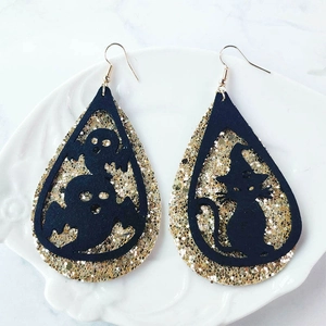Detalle de pendientes de Halloween con gatos negros fantasmas y purpurina dorada brillante