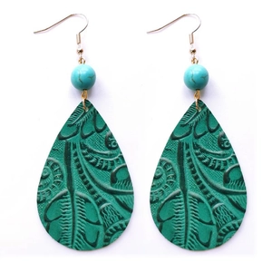 Détail de boucles d'oreilles bohèmes en cuir vert embossé avec perle turquoise et crochets