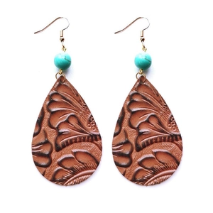Détail de boucles d'oreilles bohèmes en cuir marron gaufré avec une perle de turquoise
