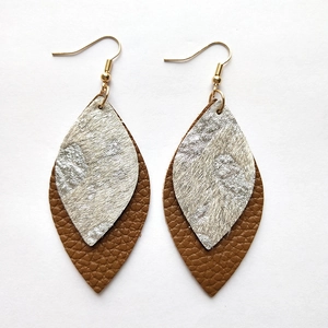 Detail of layered bohemian earrings with brown leather and silver leaf charms on white background