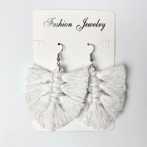 Close-up of white handmade bohemian tassel earrings with woven leaf pattern and silver hooks