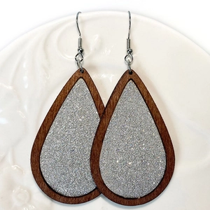 Detail van druppelvormige houten oorbellen met zilveren glitterinleg op wit bord