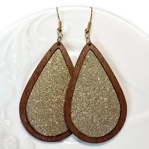 Houten waterdruppel oorbellen met gouden glitter inleg op een wit bord
