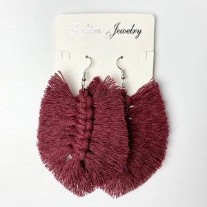 Detailed view of wine red leaf-shaped woven cotton tassel earrings on a display card