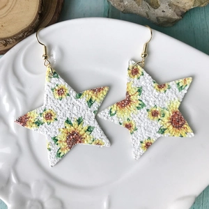 Primer plano de pendientes de cuero en forma de estrella con estampado de girasol en plato