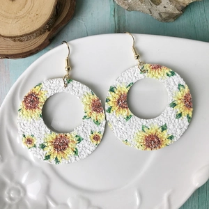Pendientes de girasol bohemios en cuero brillante con ganchos dorados sobre un plato decorado
