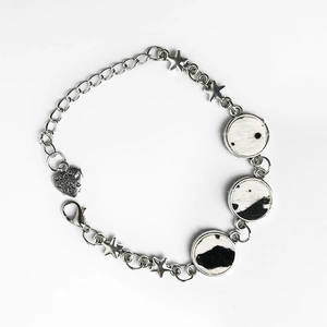 Detailed view of cow print leather charms and star pendants on a silver metal bracelet