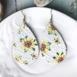 Detalle de pendientes de cuero en forma de gota con girasoles sobre un plato blanco
