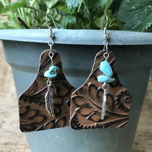 Detalle de pendientes de cuero grabado con piedras turquesas y colgantes de plumas plateadas