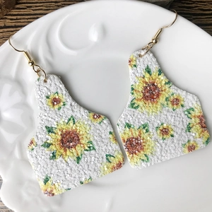 Nahaufnahme glitzernder Ohrmarke-Ohrringe mit Sonnenblumenmuster auf weißem Keramikteller