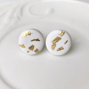 Macro view of handmade white clay stud earrings with elegant gold foil marbling effect