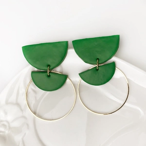 Detail van smaragdgroene klei oorbellen met gouden metalen hoepel op een wit bordje