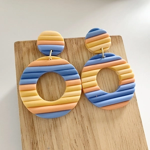 Macro shot of wavy polymer clay earrings in blue and orange on wood surface