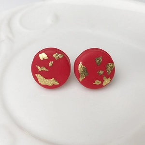 Macro shot of red handmade polymer clay stud earrings with gold leaf foil texture