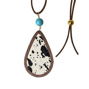 Detail of bohemian cow print wood teardrop pendant with turquoise bead on brown cord