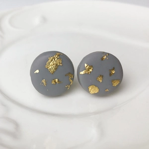 Detailed close-up of handmade gray clay stud earrings with gold foil on a white plate