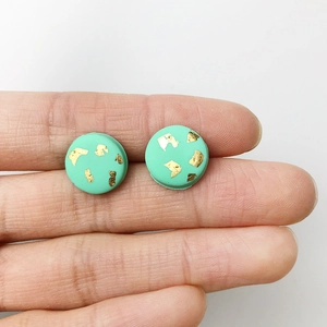 Handmade mint green clay stud earrings with gold foil accents shown on a fingertip