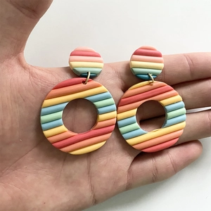 Handheld polymer clay earrings with vibrant rainbow stripes and geometric round design