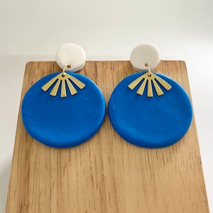 Detail of handmade clay earrings with blue discs and golden fan-shaped metal charms