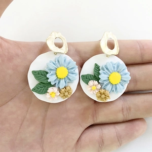 Handmade clay flower drop earrings with blue petals and golden hook on hand