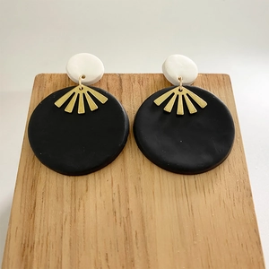 Detail of handmade black and white clay earrings with golden sunburst metal accent