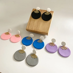 Handmade geometric clay earrings in various colors with golden accents on a wooden stand