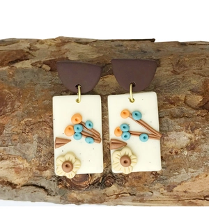 Detail of handmade clay floral earrings featuring 3D embossed daisy on rustic bark display