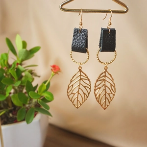 Leaf charm earrings with black leather and golden rings on a creative display
