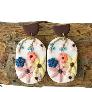 Detailed close-up of handmade polymer clay earrings with 3D floral motifs on tree bark