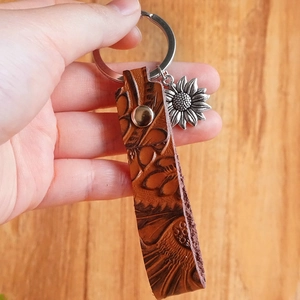 Vintage embossed leather keychain with sunflower metal pendant and dark brown texture